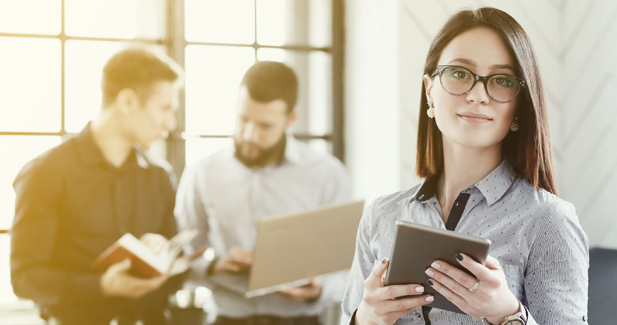 mujer de medio plano con dispositivo móvil en las manos, hombres trás conversando